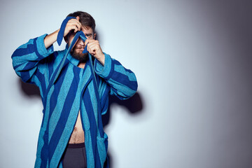 emotional man in a blue striped robe with a belt on a light background cropped view close-up