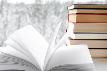 White clean pages of open book against the backdrop of old books and winter forest