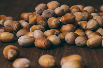Pile of nuts. Whole nuts. Hazelnuts. Corylus avellana. Macro photo, close up, on dark wooden background.