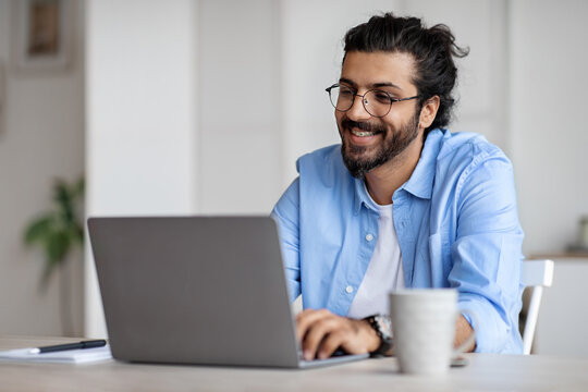 Smiling Indian Writer Using Laptop Computer, Sitting At Desk In Home Office