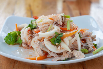 Closeup Spicy vermicelli salad in white plate on wooden table.