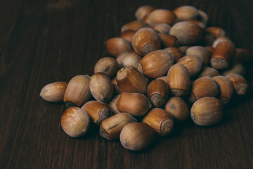 Pile of nuts. Whole nuts. Hazelnuts. Corylus avellana. Macro photo, close up, on dark wooden background.