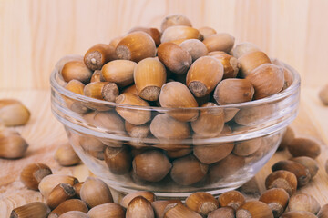 Hazelnuts in glass bowl. Whole nuts. Corylus avellana. Close up, on wooden background.