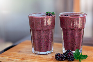 Delicious blackberry smoothie with mint and fresh berries in glasses on wood desk and grey background. Healthy lifestyle concept