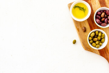 Green and black olives, olive oil in bowls on cutting board top-down copy space