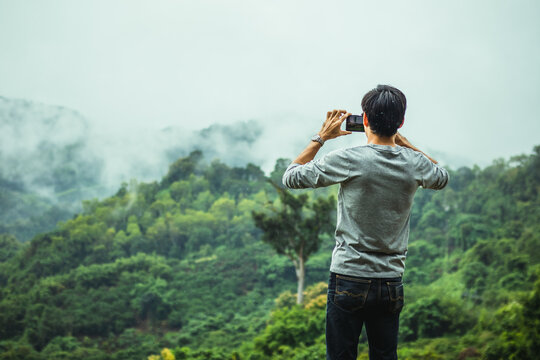 Asian male tourists take pictures of mountain landscapes after rain in northern Thailand.