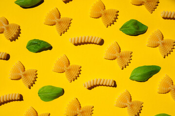Uncooked curly pasta and basil leaf pattern on yellow background. Traditional dry raw macaroni pattern. Nobody