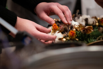 Christmas wreath weaving workshop. Woman hands decorating holiday wreath made of spruce branches, cones and various organic decorations on the table