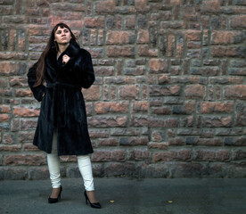Young woman in a black mink coat near a stone wall. Beauty and fashion concept.