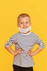 Portrait of cute little child boy wearing protective mask on yellow background. Virus protection and healthcare concept during COVID pandemic