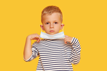 Portrait of cute little child boy wearing protective mask on yellow background. Virus protection and healthcare concept during COVID pandemic