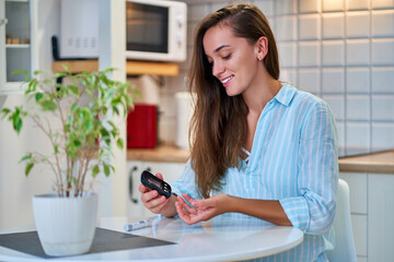 Young woman checks and measures blood glucose level using glucose meter. Treatment and controlling...