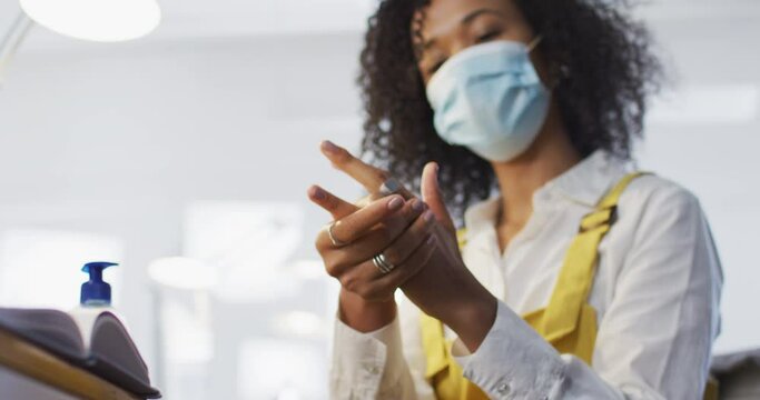 African American woman wearing face mask sanitizing her hands at office