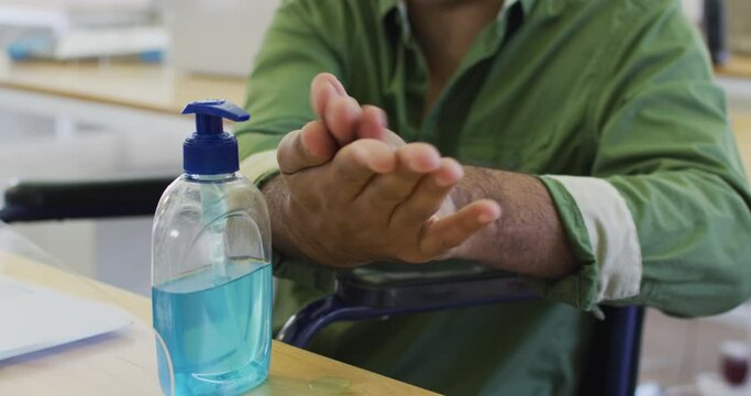 Mixed race man wearing face mask sanitizing his hands at office