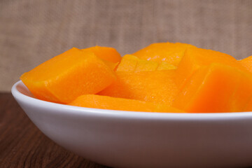Pieces of pumpkin in the bowl at the wooden table and sackcloth background.