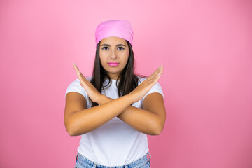 Naklejka premium Young beautiful woman wearing pink headscarf over isolated pink background Rejection expression crossing arms doing negative sign, angry face