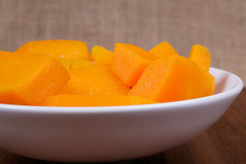 Pieces of pumpkin in the bowl at the wooden table and sackcloth background.