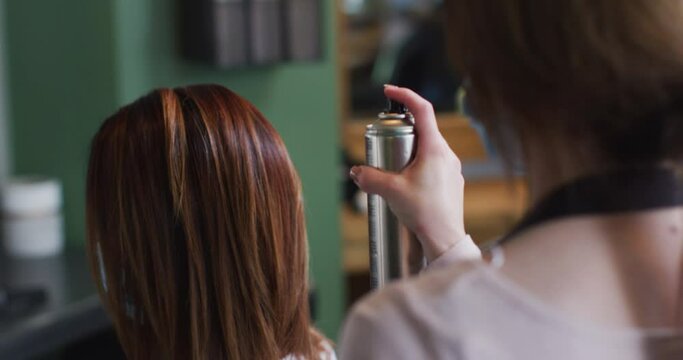 Female hairdresser spraying hairspray on hair of female customer at hair salon