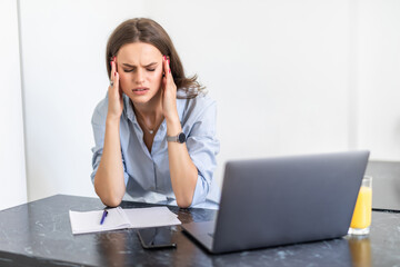 Young tired woman sitting in front of laptop while touching her forehead during work over project