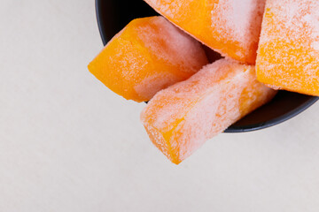 Frozen pieces of pumpkin in the black bowl at tablecloth.