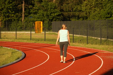 Fototapeta premium A woman runs on the treadmill of a stadium around a football field. Artificial cover of the sports complex. Activity for weight loss and a healthy lifestyle. Preparing for the competition. Free time