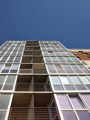 Fototapeta premium Lviv, Ukraine - 3 4 2020: Facade of a tall multi-storey modern house with balconies and large glass windows. Design of modern architecture. Top view from the bottom. Modern city architecture