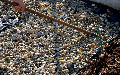 delivery of gray river pebbles like mulch to flower beds in the garden using a wheelbarow from the body of a truck or trailer. shovel and rake the layer over the black nonwoven fabric.