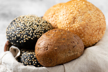 Sesame buns for burgers. Wheat and rye buns in a basket on a light gray background. Homemade buns with sesame seeds. Baking close-up