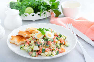 Salad with red fish, fresh cucumbers and herbs, an egg on a white plate with white bread toasts, selective focus