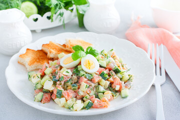 Salad with red fish, fresh cucumbers and herbs, an egg on a white plate with white bread toasts, selective focus
