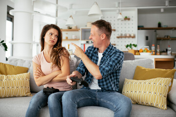 Obraz premium Husband and wife playing video game with joysticks in living room. Loving couple are playing video games at home.