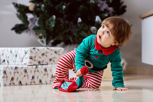 A little 12-month-old Christmas elf with a Christmas tree and gifts