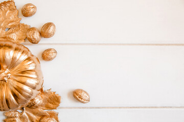 Pumpkin, leaves and nuts painted in gold on a white wooden background. Flat layout with space for text