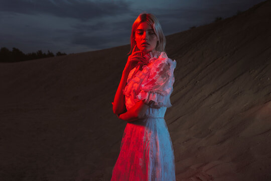 Woman in a long dress standing near a sandy hill in the evening