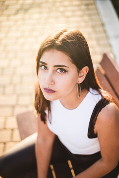 Teenager wit intense gaze and big eyes sitting on a bench at sunset