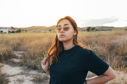 Teenager with sunglasses touching hair at sunset in the countryside