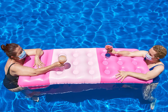 Two women bathe in a pool with a sanitary mask. They maintain the safety distance.