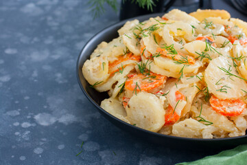 Baked potatoes with carrots in the oven on a black dish, selective focus, copy space