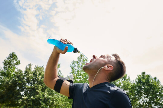 Man drinking sports drink after training. He is in an outdoor park.