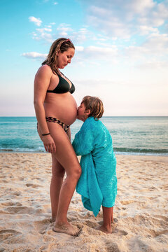 5 years old kid kissing the belly of his pregnant mother, at the beach