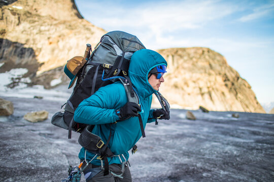 Mountaineer lifts heavy backpack onto shoulders while crossing glacier