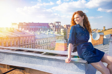 Fototapeta premium Portrait of a red-haired woman on the roof of the city, a girl walking under the roofs. Copy Space