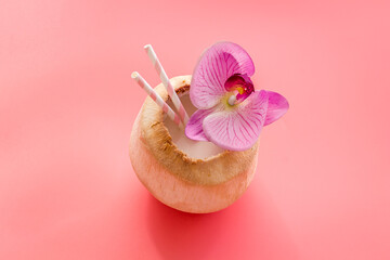 Raw coconut water or milk with straw and orchid flower, above view