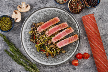 grilled tuna steaks on a modern plate with a salad of mushrooms,vegetables and sesame seeds, top view