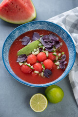 Blue plate with gazpacho cold soup made of red tomatoes and watermelon, vertical shot on a grey concrete background