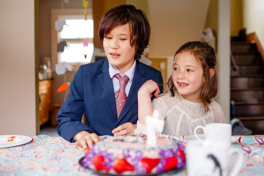 two smiling children sit at a table in front of lit birthday cake