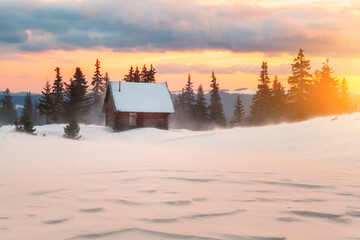 Fantastic winter landscape with wooden house in snowy mountains. Hight mountain peaks in foggy sunset sky. Christmas and winter vacations holiday concept