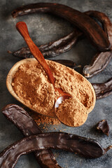 Dry carob powder and pod in a wooden bowl close up