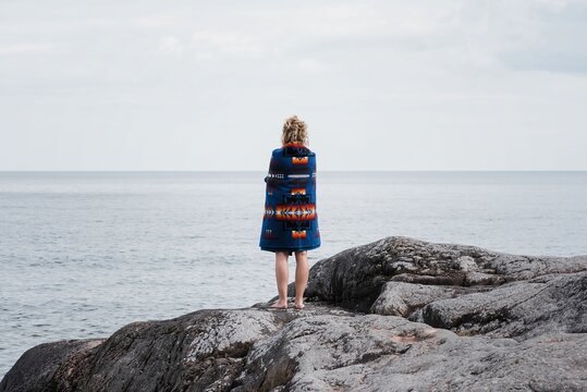 woman standing on rocks wrapped in a Pendleton blanket in Sweden