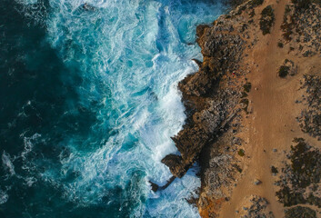 Aerial top view of sea waves hitting rocks on the beach with turquoise
